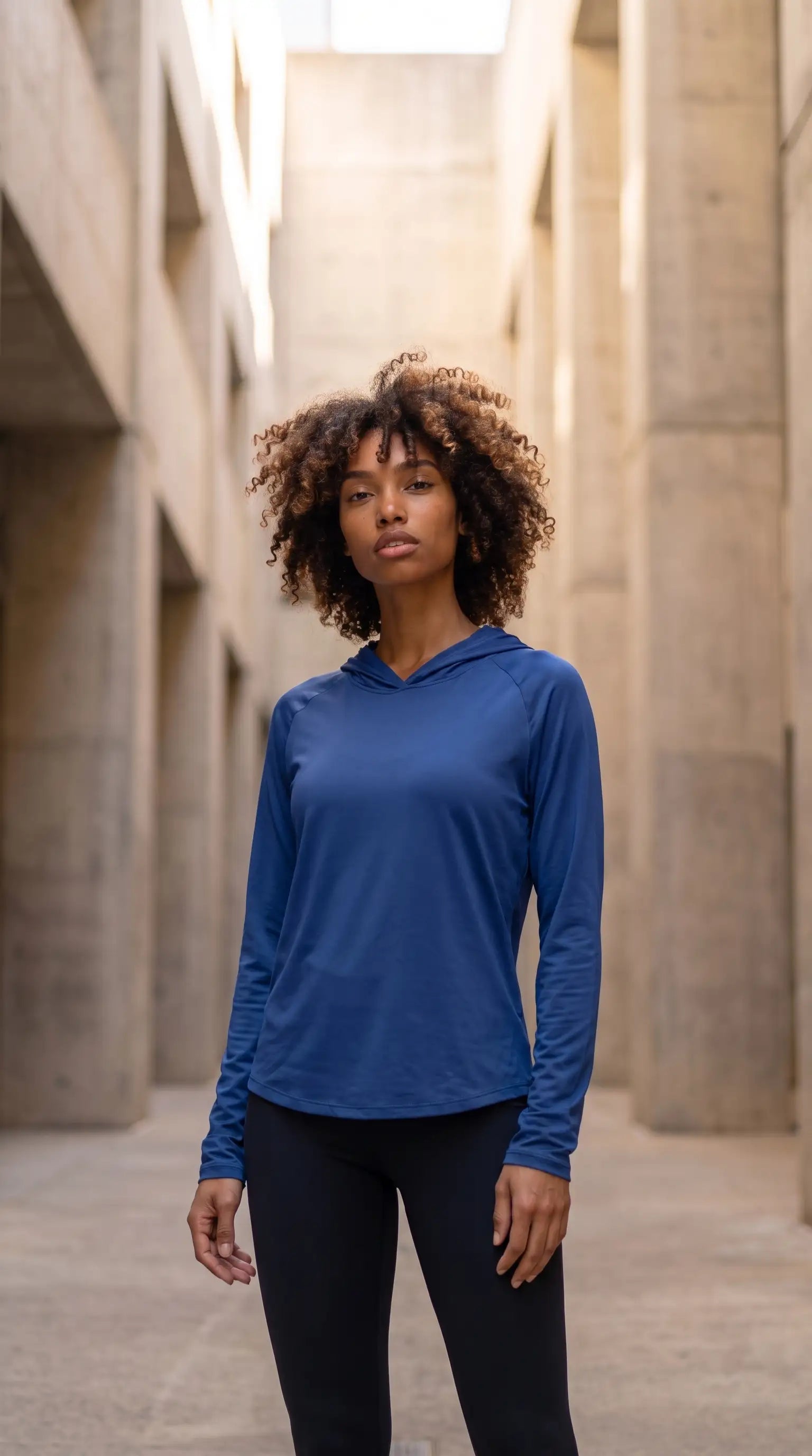 Women's hooded sun protection running shirt worn by a model in a modern outdoor setting.