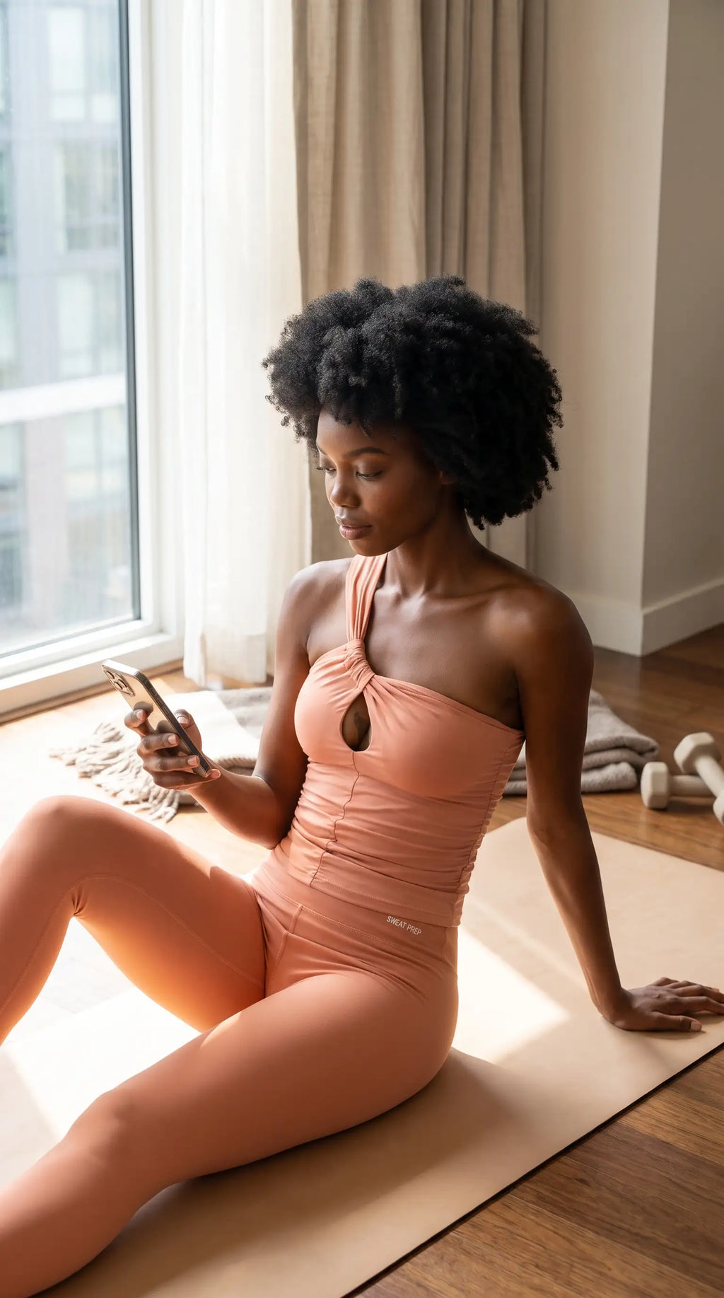 Model wearing a Premium & High-End Teacup Yoga Top, seated on a yoga mat and checking her phone.
