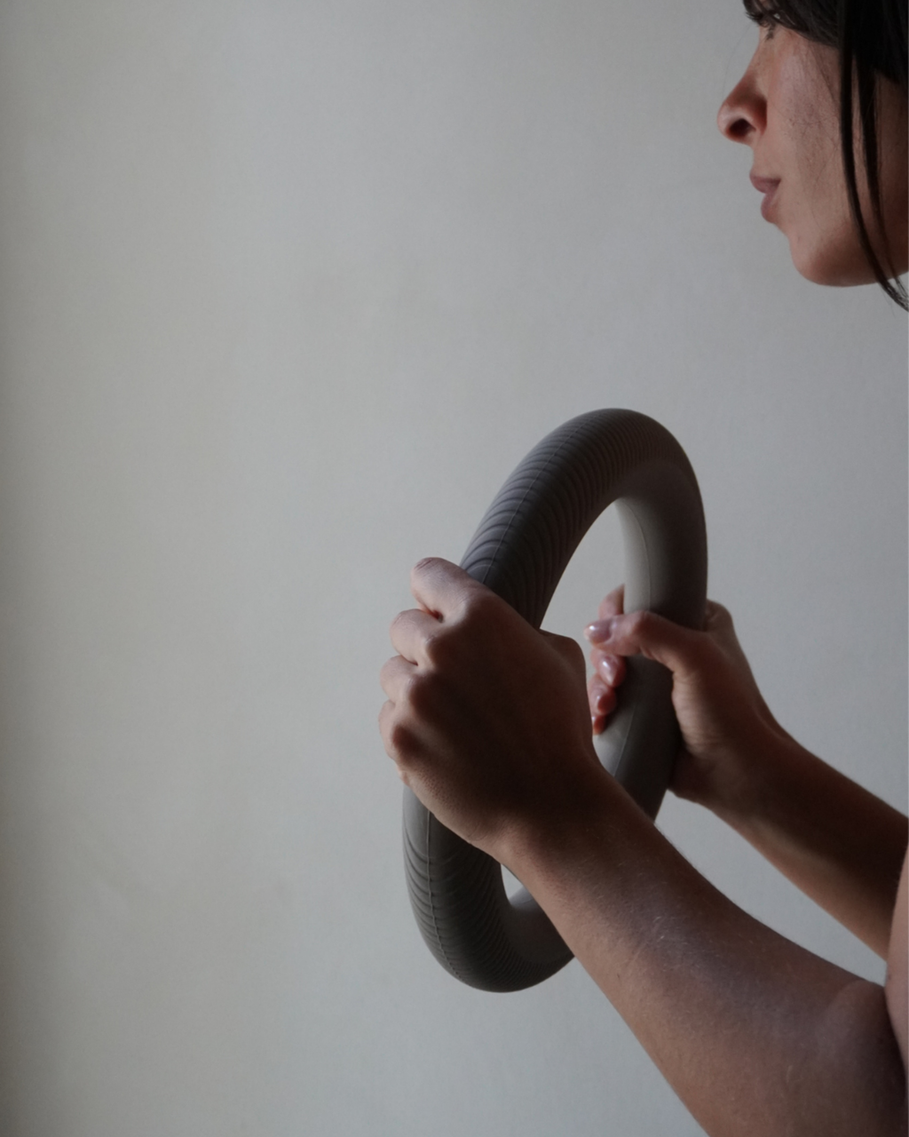 Close-up of hands holding the MUNA ring-shaped dumbbell for home workouts against a neutral background.