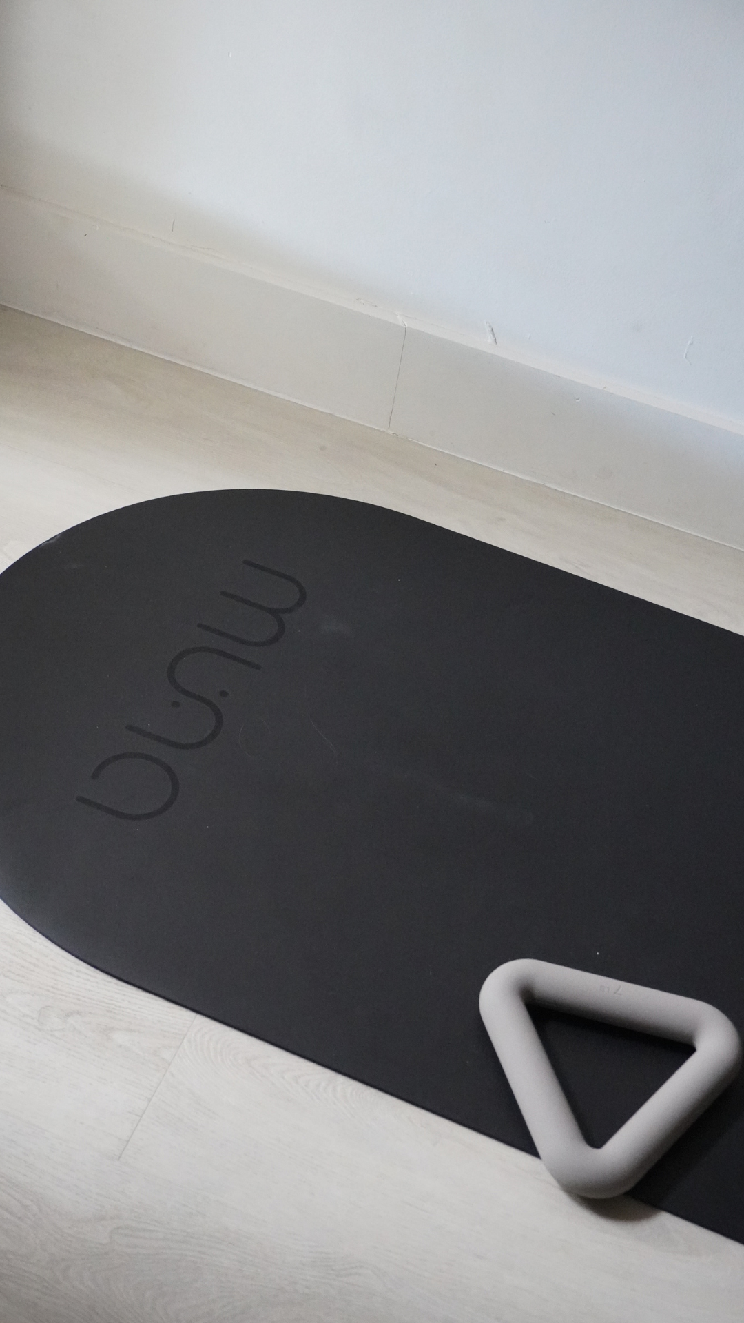 MUNA Oval Yoga Mat in black with non-slip performance and a light gray yoga accessory on a wooden floor.