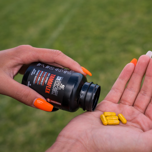 Hand pouring TAMAFLEX SUPPLEMENT ESSWENTIAL capsules into palm, showcasing the product for athletes.