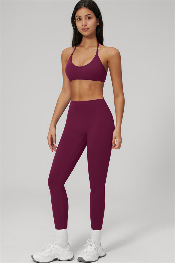 Model wearing The Rapture Sports Bra Leggings 2-Piece Set in burgundy color, showcasing a halter neckline and high-waisted leggings.