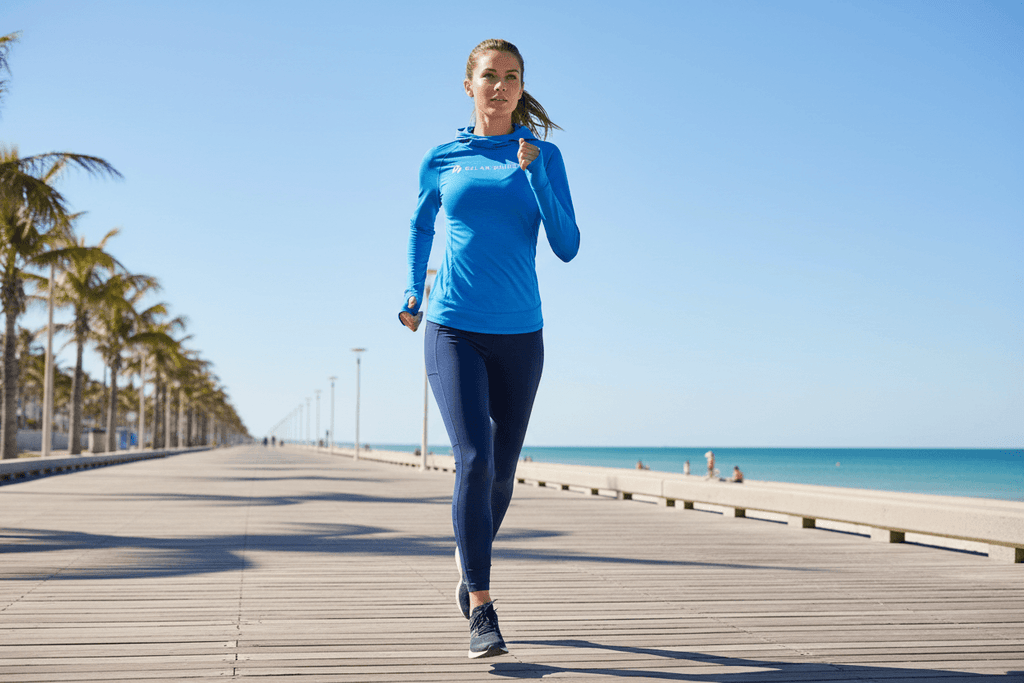 Women's Hooded Sun Protection Running Shirt – UPF Long Sleeve Athletic Top worn by a woman jogging on a sunny boardwalk.